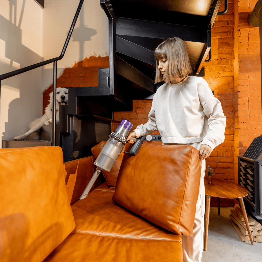 woman vacuuming sofa with dog in background 