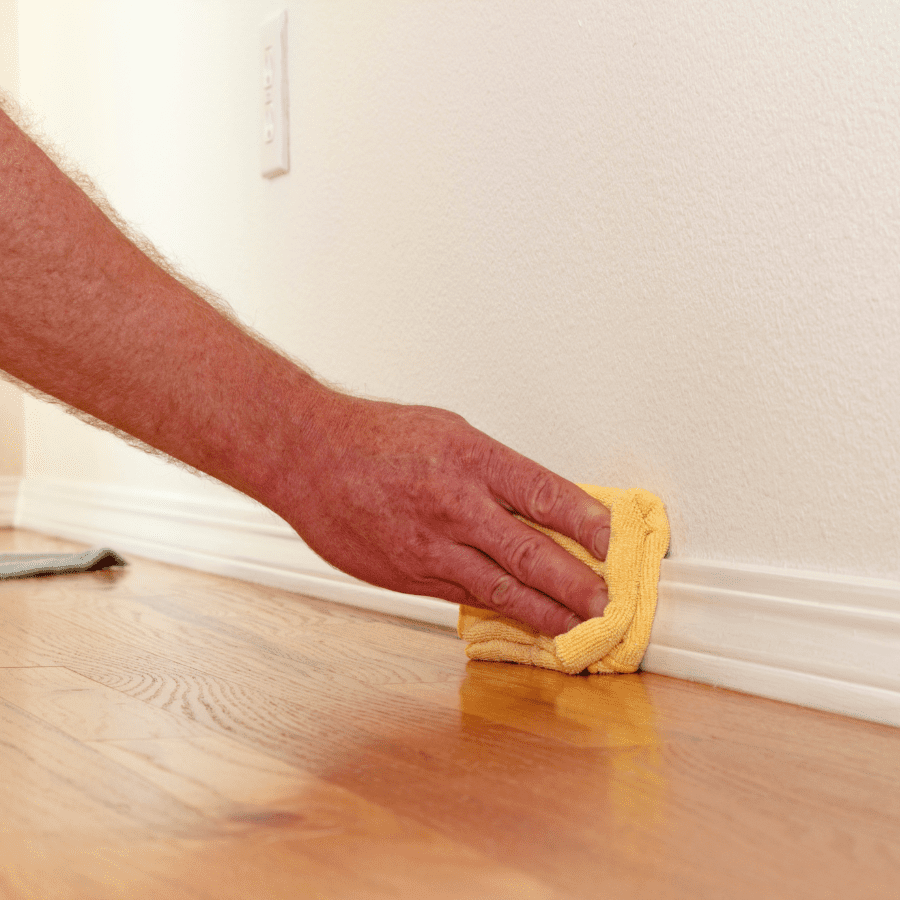 hand wiping a baseboard with microfiber towel 